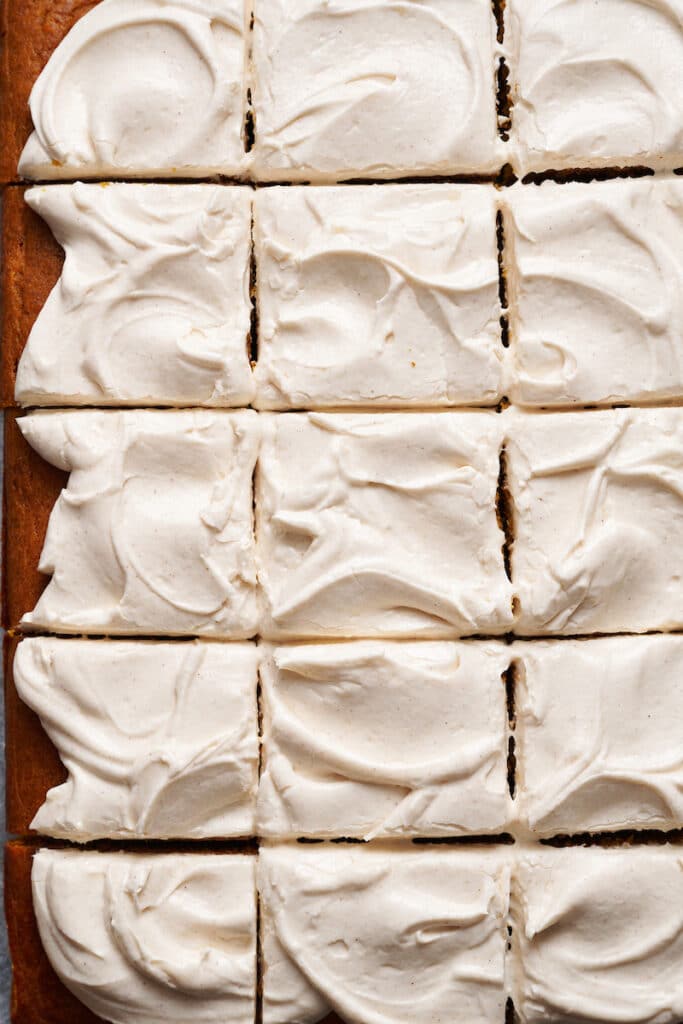 Pumpkin cake topped with cream cheese frosting cut into squares. 