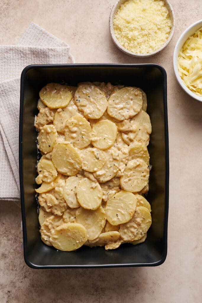 Thinly sliced potatoes in a black casserole dish.