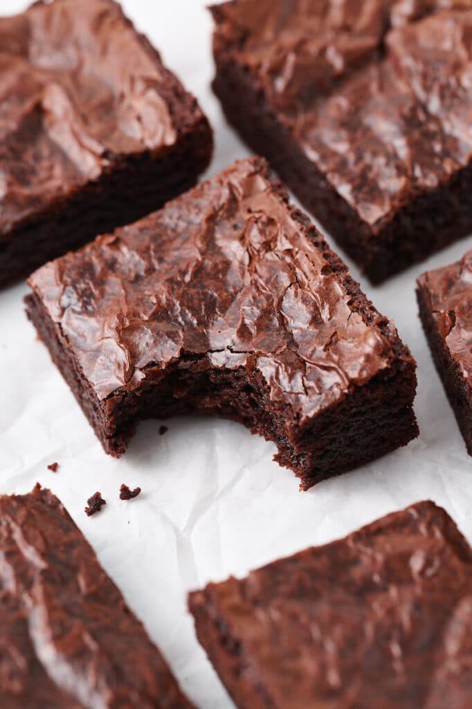 Brownies cut up on a white piece of parchment paper with a bite taken out of it. 