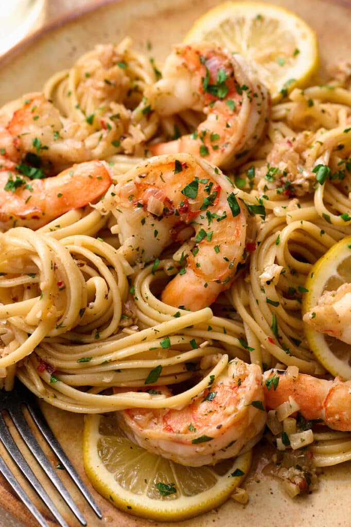 Shrimp scampi on a beige plate with wine on the side.