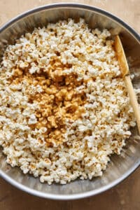 Combining the caramel sauce with the popped popcorn to create caramel corn.