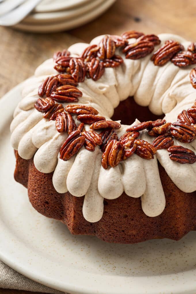 pumpkin bundt cake on a serving platter with cream cheese frosting and pecans.