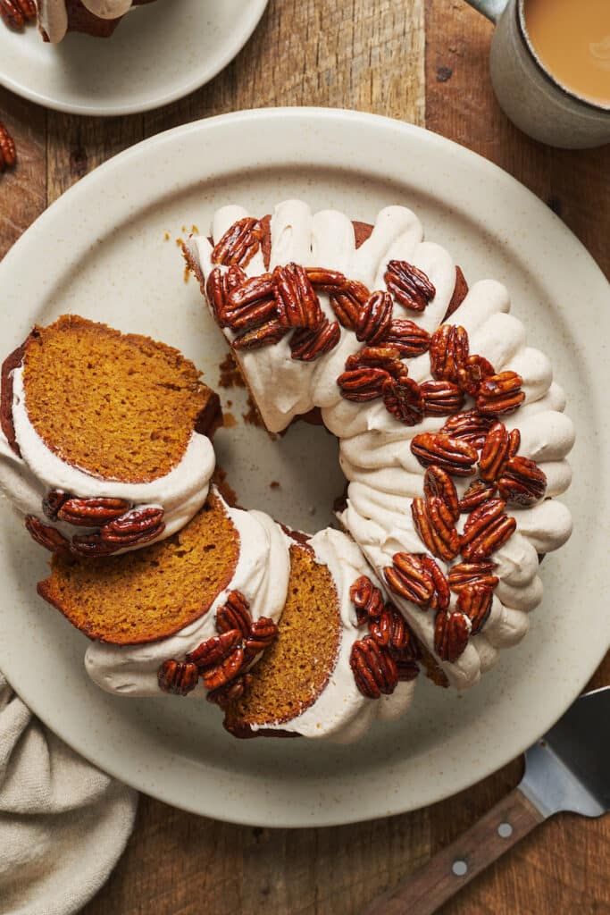 Pumpkin bundt cake topped with cream cheese frosting and pecans on a large plate. 