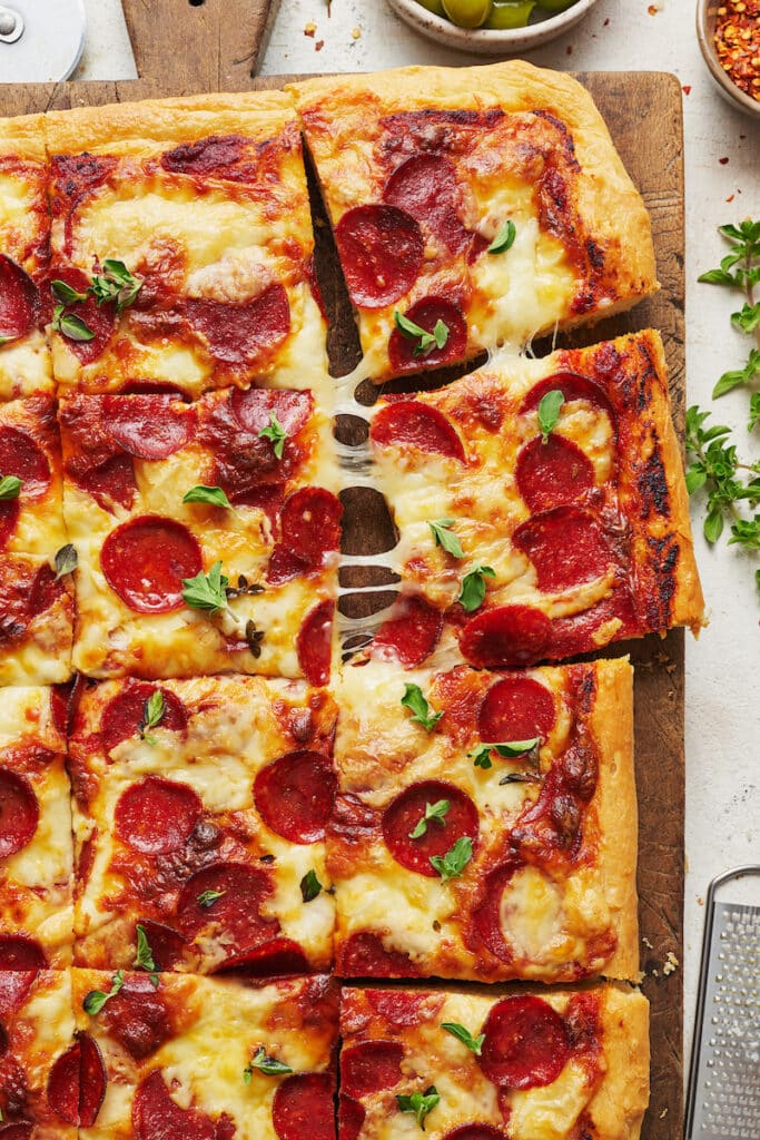 Pepperoni pizza cut into slices on a wooden cutting board. 