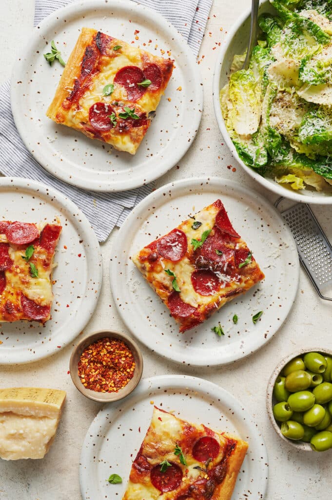 Slices of pepperoni pizza on white plates with salad on the side.