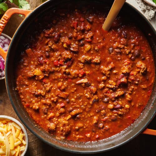 A dutch oven with homemade chili in it. Chili toppings on the table below.