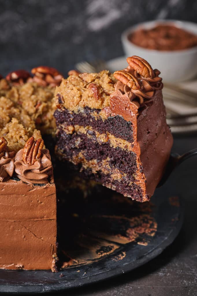 Slice of German Chocolate cake being removed from platter with cake server. 