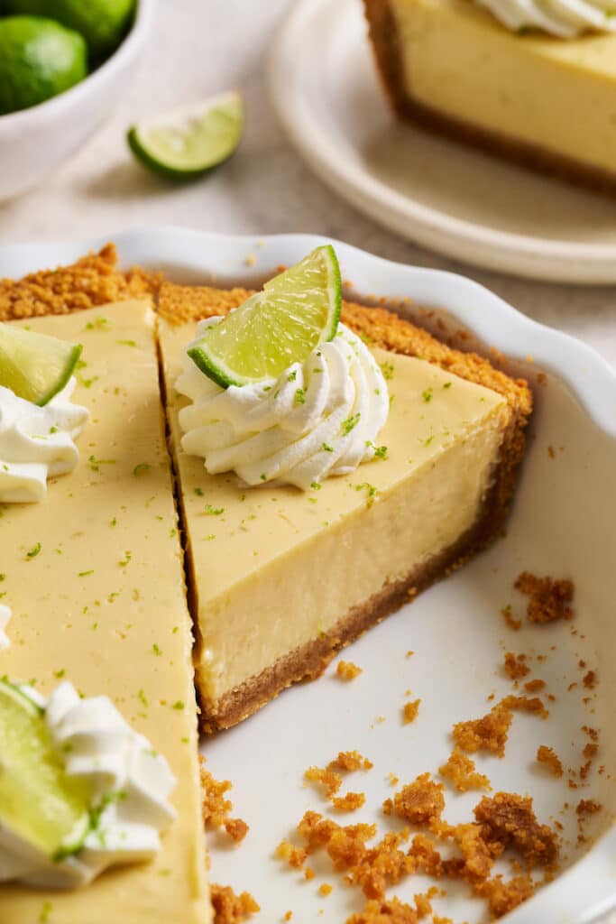 Slice of key lime pie in pie plate with whipped cream on top.