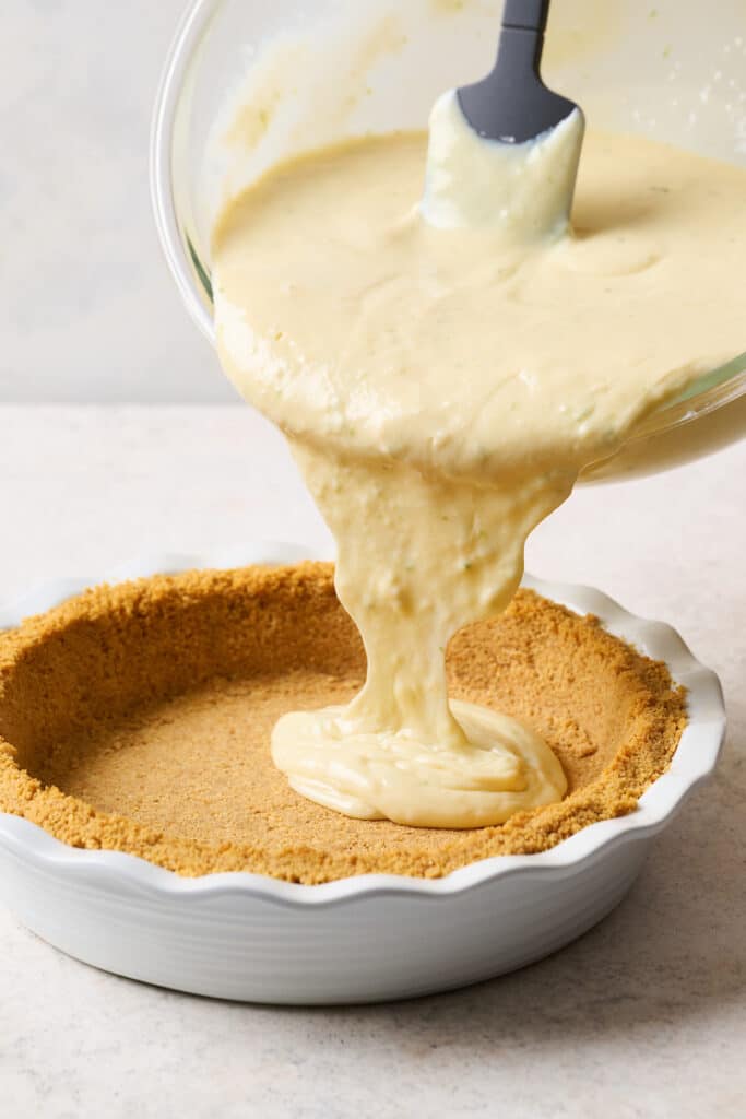 Key lime pie filling being poured into the graham cracker crust. 