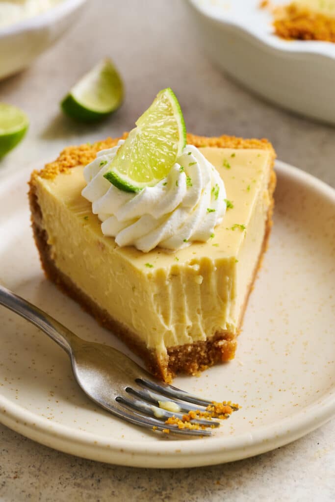 Slice of key lime pie on a dessert plate with a bite taken out of it.