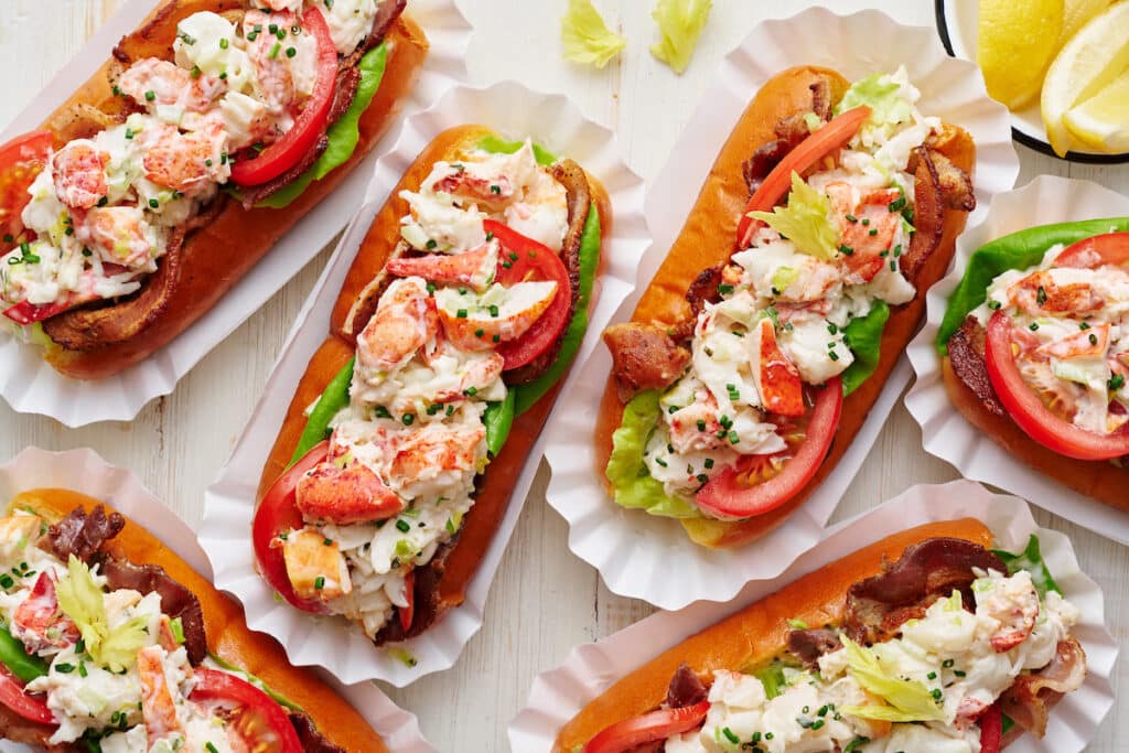 Learn how to make lobster rolls with this easy lobster roll recipe! The lobster salad contains cooked lobster meat, lemon juice, melted butter, mayo, and fresh herbs. The lobster mixture is piled high on toasted split top buns and topped with bacon, lettuce, and tomato! We love to serve these with crunchy potato chips and ice cold beer.