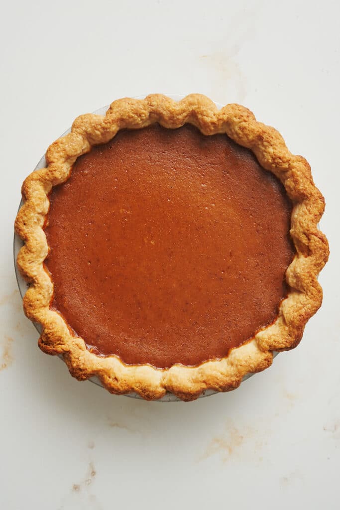 Bourbon pumpkin pie with pie crust in pie plate on white table.