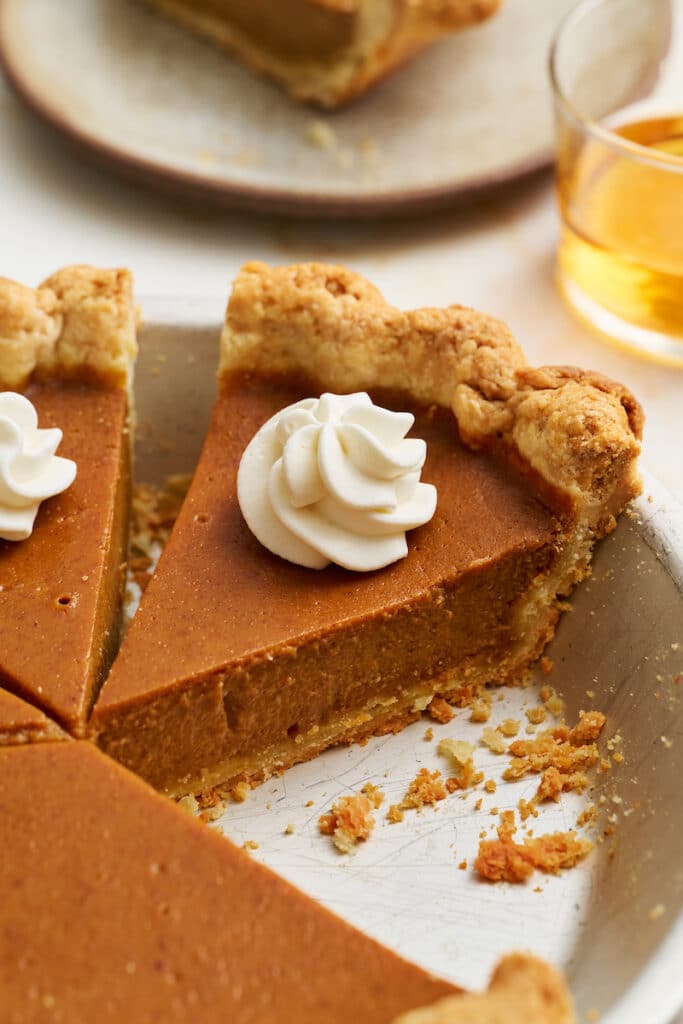 Bourbon pumpkin pie slice in pie plate with whipped cream on top.