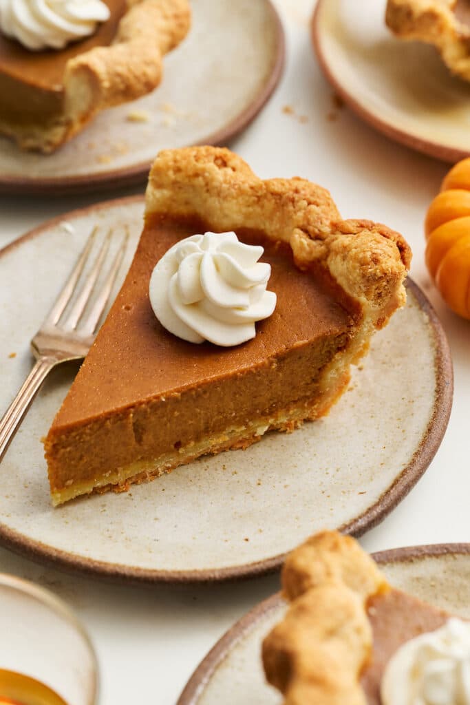 A slice of bourbon pumpkin pie on a dessert plate with whipped cream on top!!! 