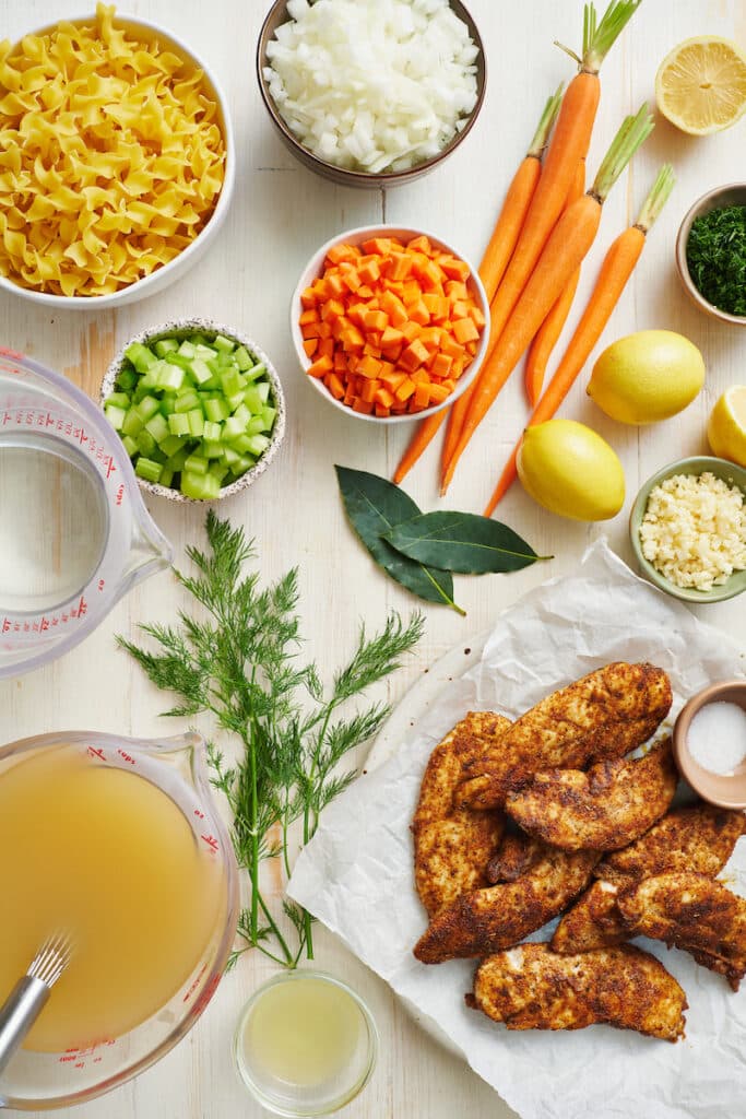 Ingredients for classic chicken noodle soup on a white table.