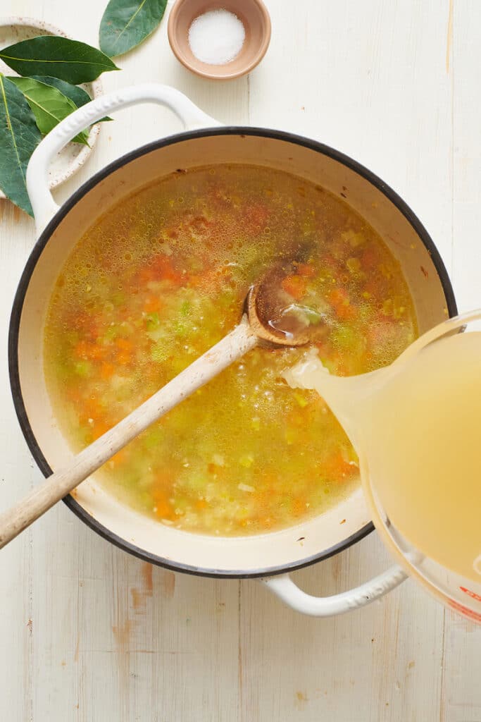 Pouring chicken broth into stockpot for chicken noodle soup recipe.