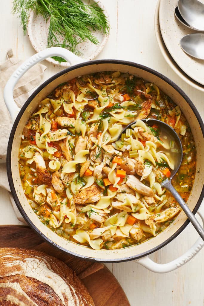 Big pot of chicken noodle soup in dutch oven with ladle. 