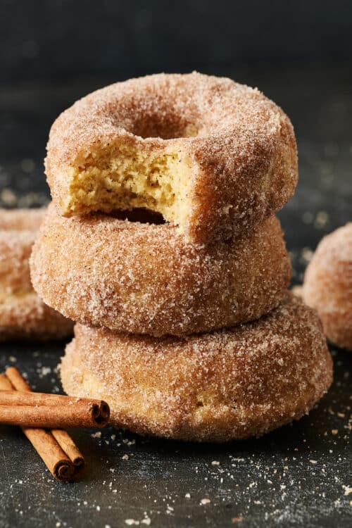 Stack of cinnamon sugar donuts with cinnamon sticks on the side.