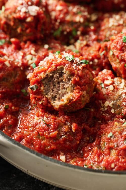 Meatballs in a dutch oven with marinara sauce and cheese on top.