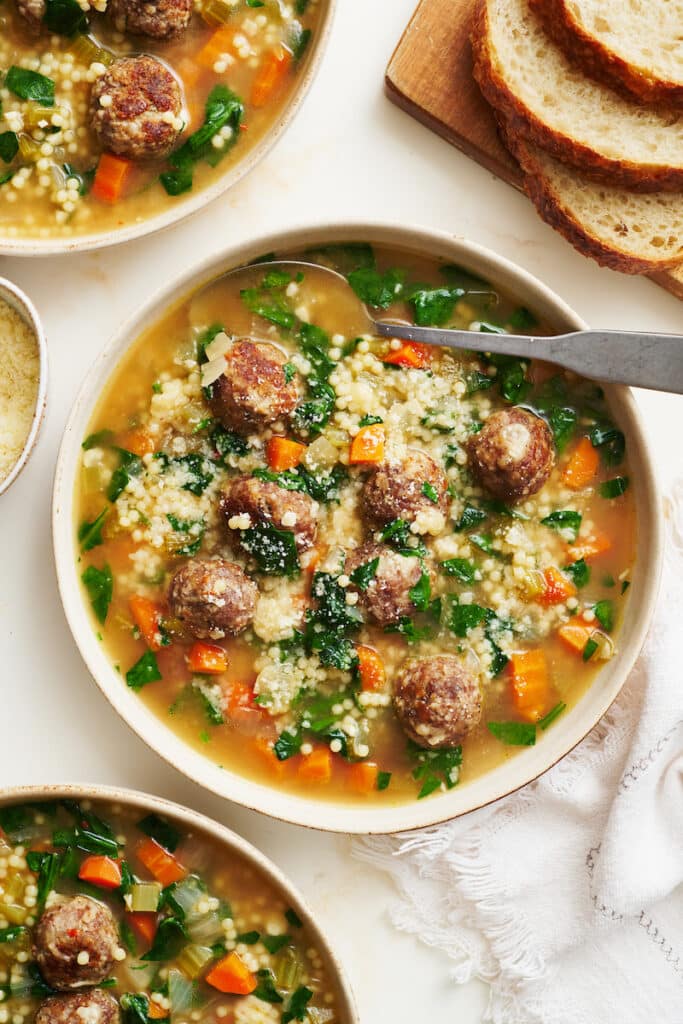 Bowl of wedding soup with cheese on top and bread on the side.