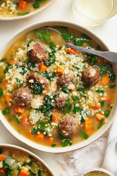 Bowl of Italian wedding soup with cheese on top.