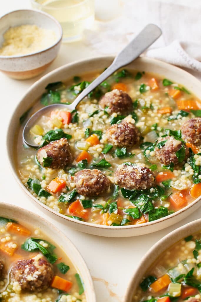 A bowl of Italian wedding soup with cheese on top.