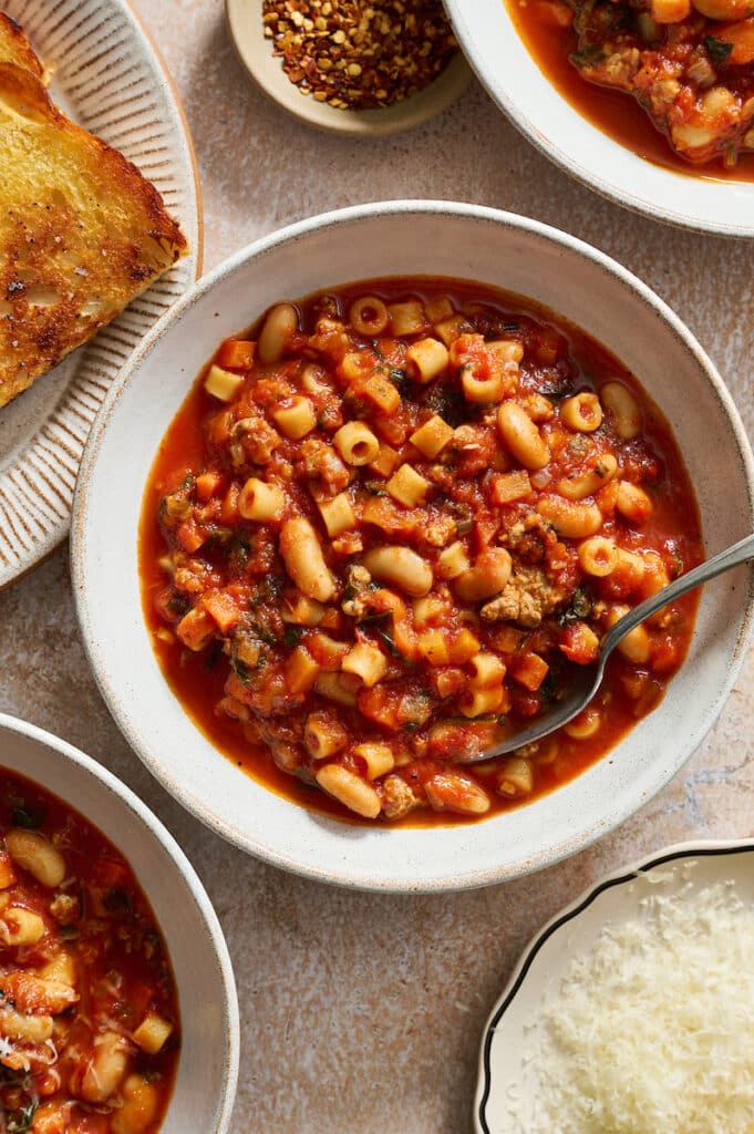 White bowl of pasta fagioli soup with Parmesan cheese on the side.