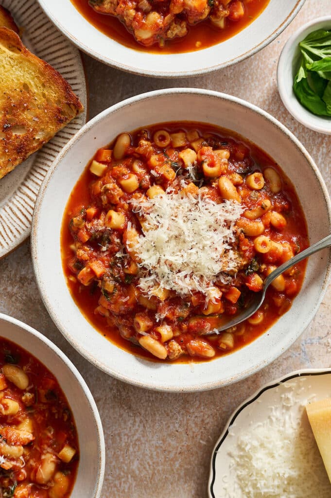 White bowl with pasta fagioli soup and freshly grated Parmesan cheese.