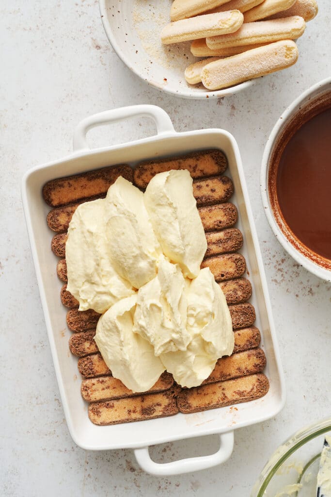 Lady fingers in a baking dish topped with mascarpone filling.