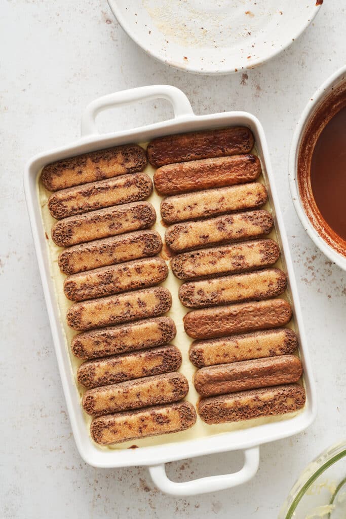 Lady fingers dipped in espresso mixture arranged in baking dish.