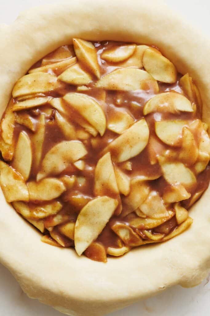 A slice of homemade apple pie with apple pie filling and a flaky pie crust plus vanilla ice cream.