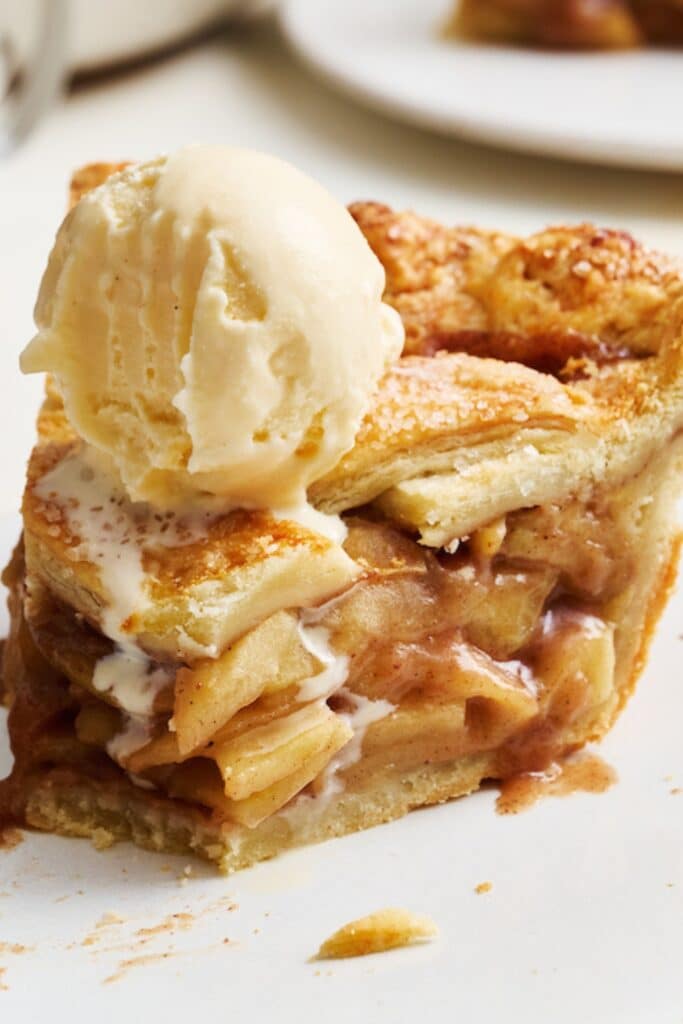 A slice of homemade apple pie with apple pie filling and a flaky pie crust plus vanilla ice cream.