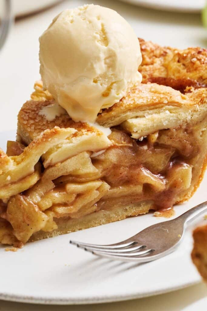 A slice of homemade apple pie with apple pie filling and a flaky pie crust plus vanilla ice cream.
