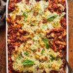 Casserole dish full of baked ziti topped with cheese and basil.