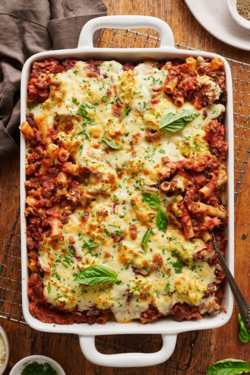 Casserole dish full of baked ziti topped with cheese and basil.