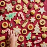 Christmas cookies on a red table with a hand picking up a cookie.