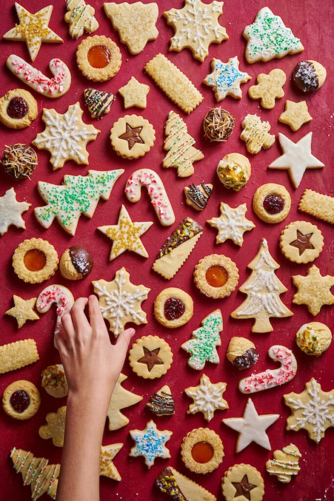 Christmas cookies on a red table with a hand picking up a cookie.