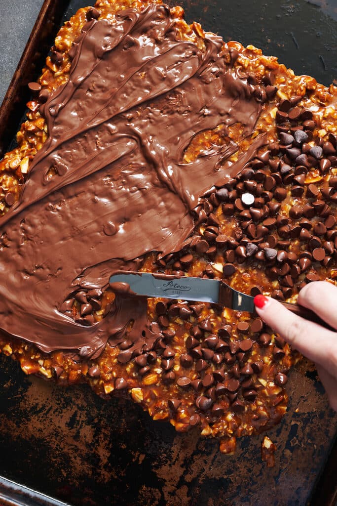 Spreading chocolate chips on top of toffee. 