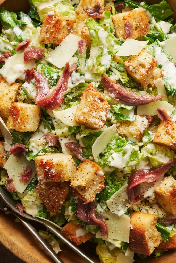 A big bowl of homemade Caesar salad topped with anchovies and croutons.