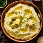 Fluffy sour cream Mashed Potatoes in a large bowl topped with melted butter and chives.