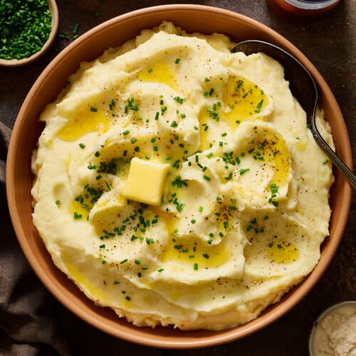 Fluffy sour cream Mashed Potatoes in a large bowl topped with melted butter and chives.