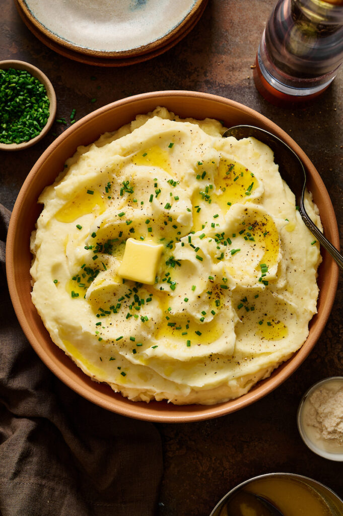 Fluffy sour cream Mashed Potatoes in a large bowl topped with melted butter and chives.