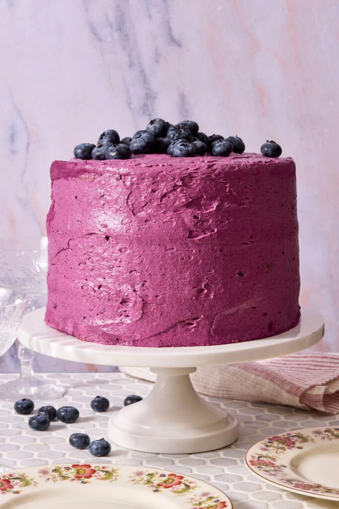 A triple layer lemon blueberry cake covered with blueberry frosting and topped with fresh blueberries.