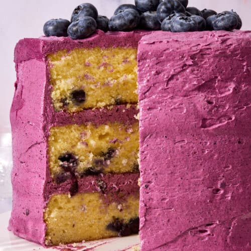 A triple layer lemon blueberry cake covered with blueberry frosting and topped with fresh blueberries.