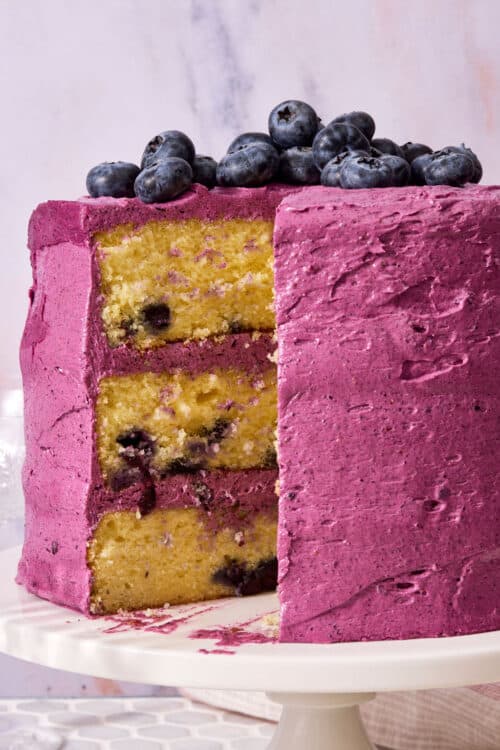 A triple layer lemon blueberry cake covered with blueberry frosting and topped with fresh blueberries.