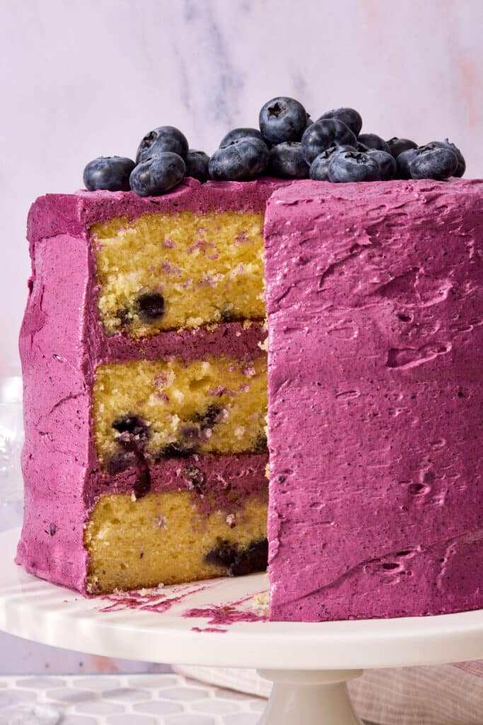 A triple layer lemon blueberry cake covered with blueberry frosting and topped with fresh blueberries.