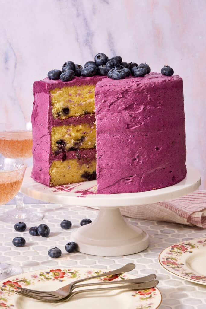 A triple layer lemon blueberry cake covered with blueberry frosting and topped with fresh blueberries.