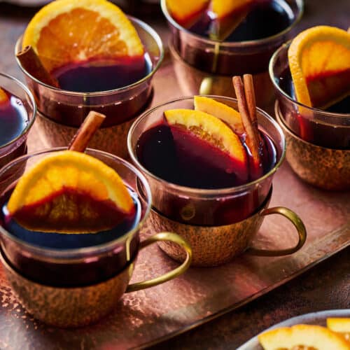Mulled wine in brass glasses with orange slices and cinnamon sticks.