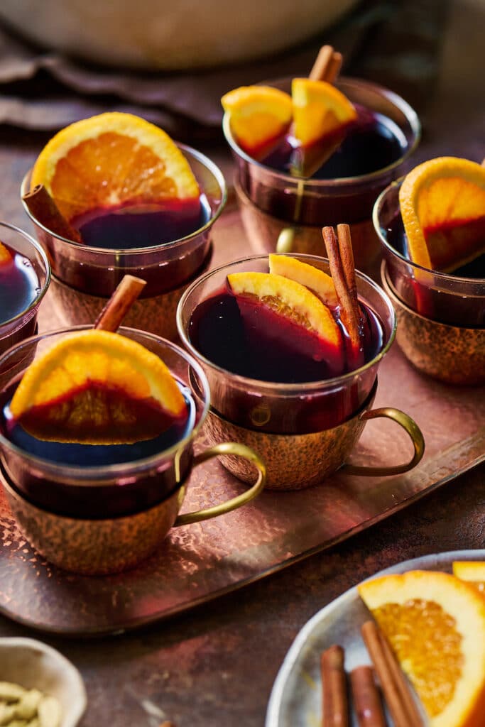 Mulled wine in brass glasses with orange slices and cinnamon sticks.